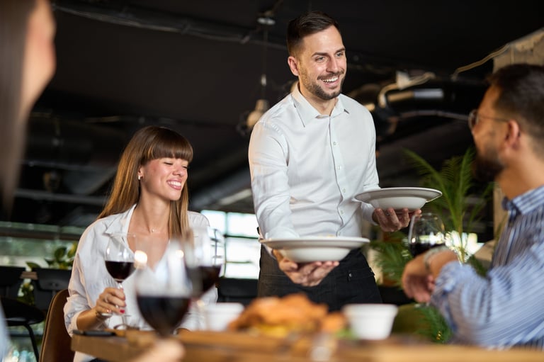Happy waiter serving group of business people during lunch time