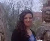 Woman with long dark hair wearing a blue jacket, standing outdoors near a brick wall on a gray day