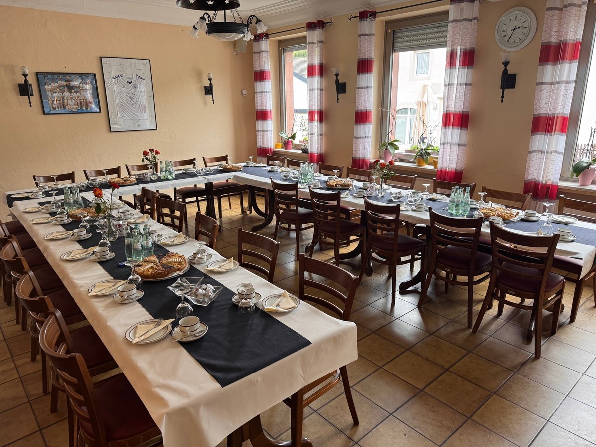 Festlich eingedeckter Saal mit langen Tischen, weißen Tischdecken, schwarzen Servietten und floralen Gestecken
