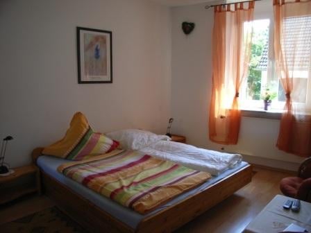 Cozy bedroom with wooden bed featuring colorful striped bedding, orange curtains on window, and bedside furniture